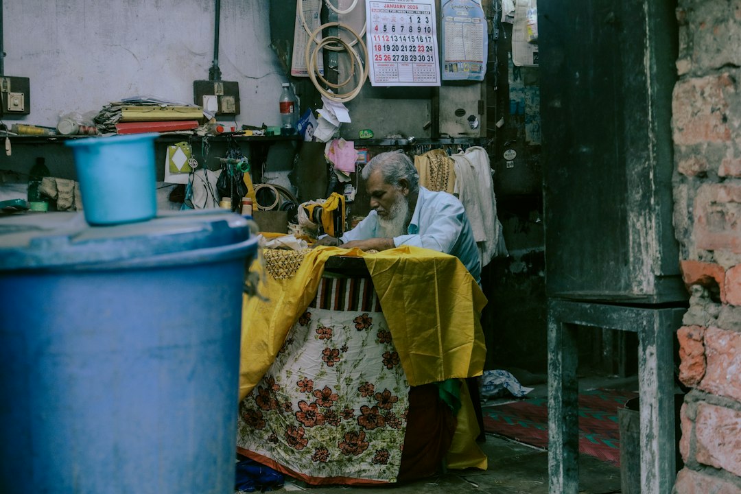 Elderly man sewing at a table in a cluttered room