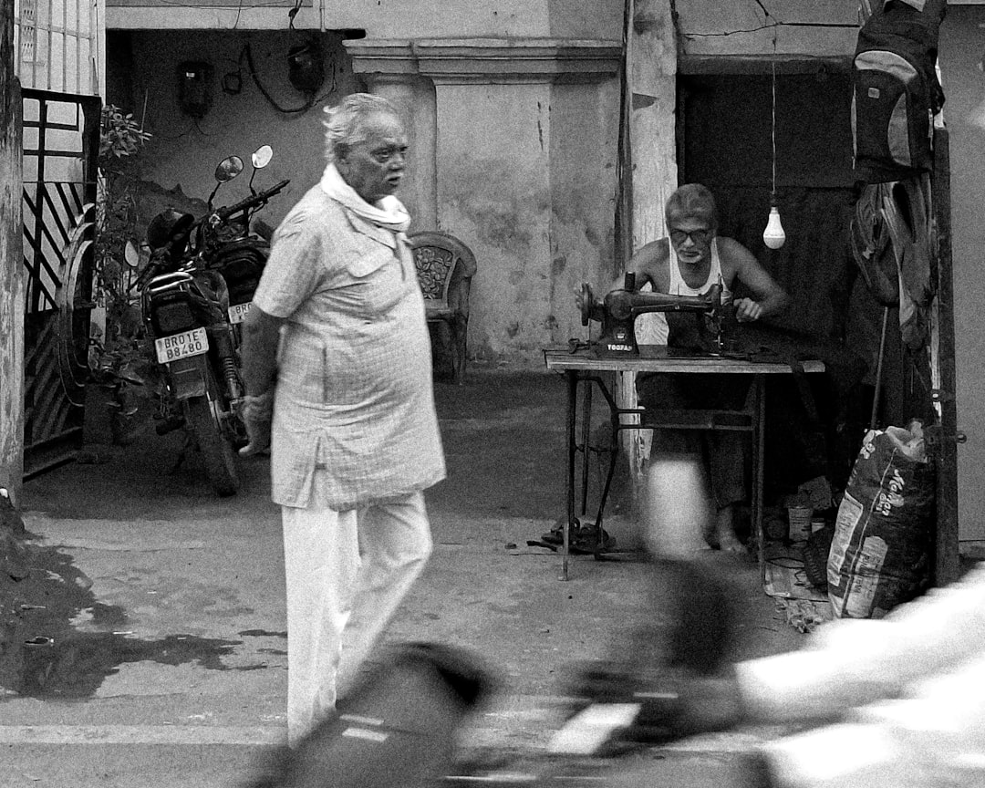 Elderly man walking past tailor working on sewing machine